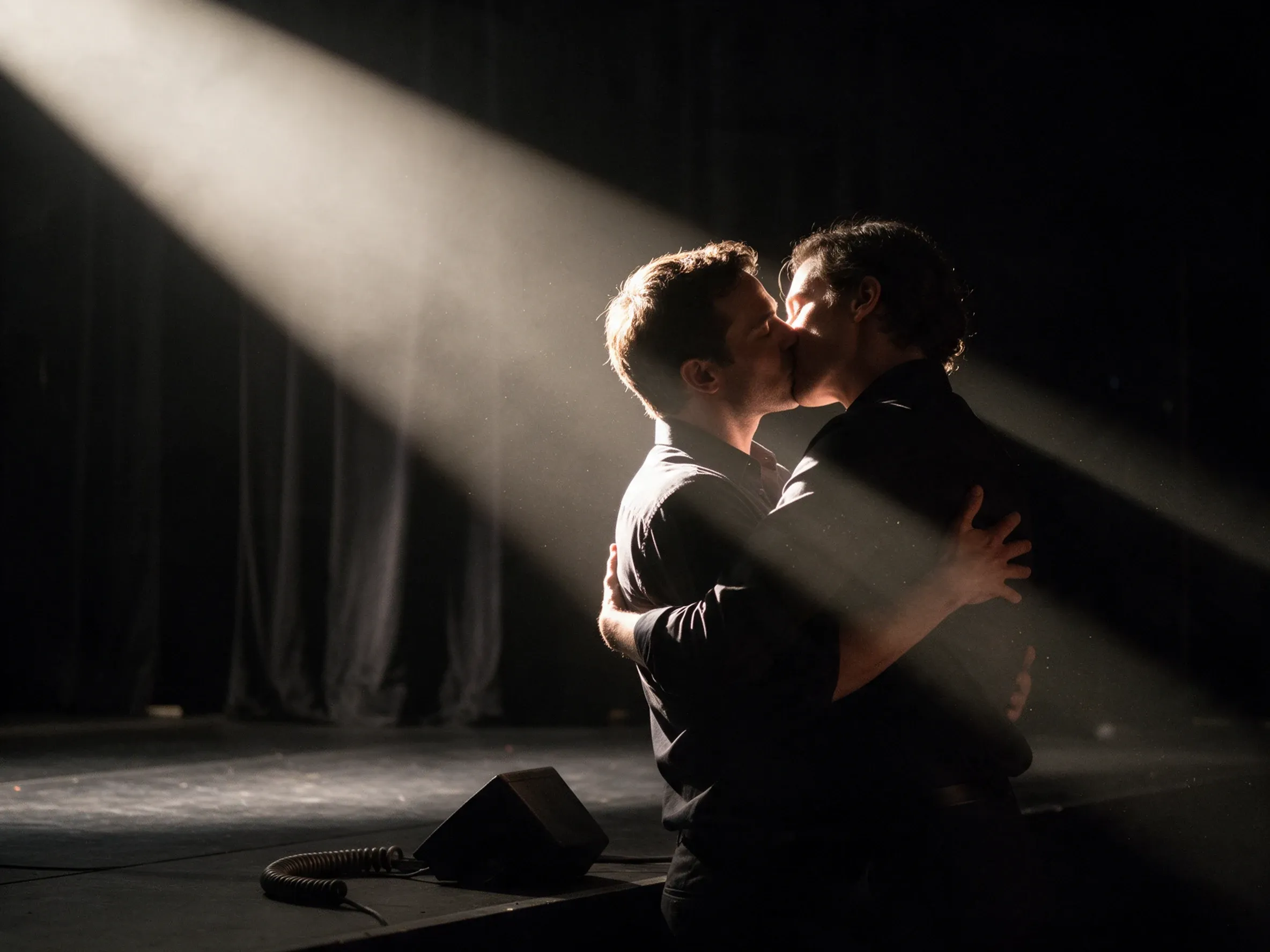 Couple embracing and kissing in the edge of a stage spotlight in a dark venue